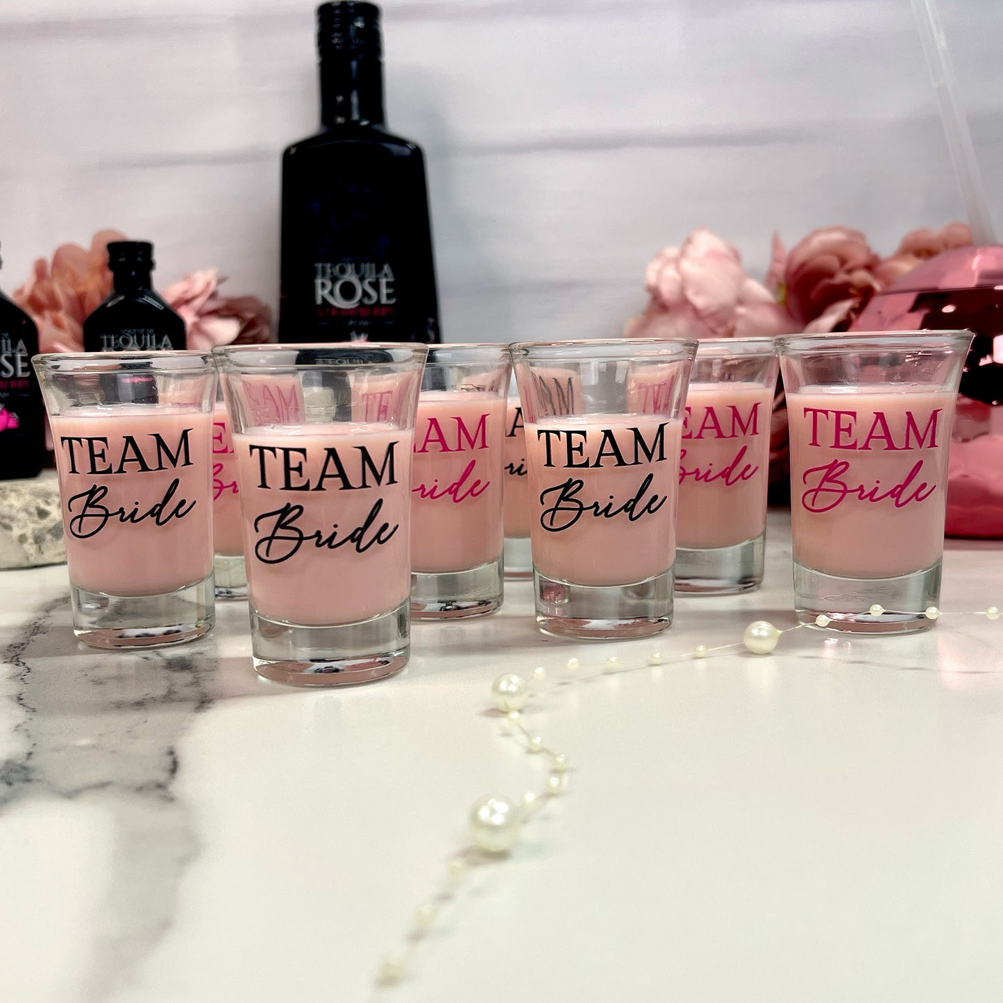 Set of shot glasses with 'Team Bride' text on a table with tequila bottles in the background.