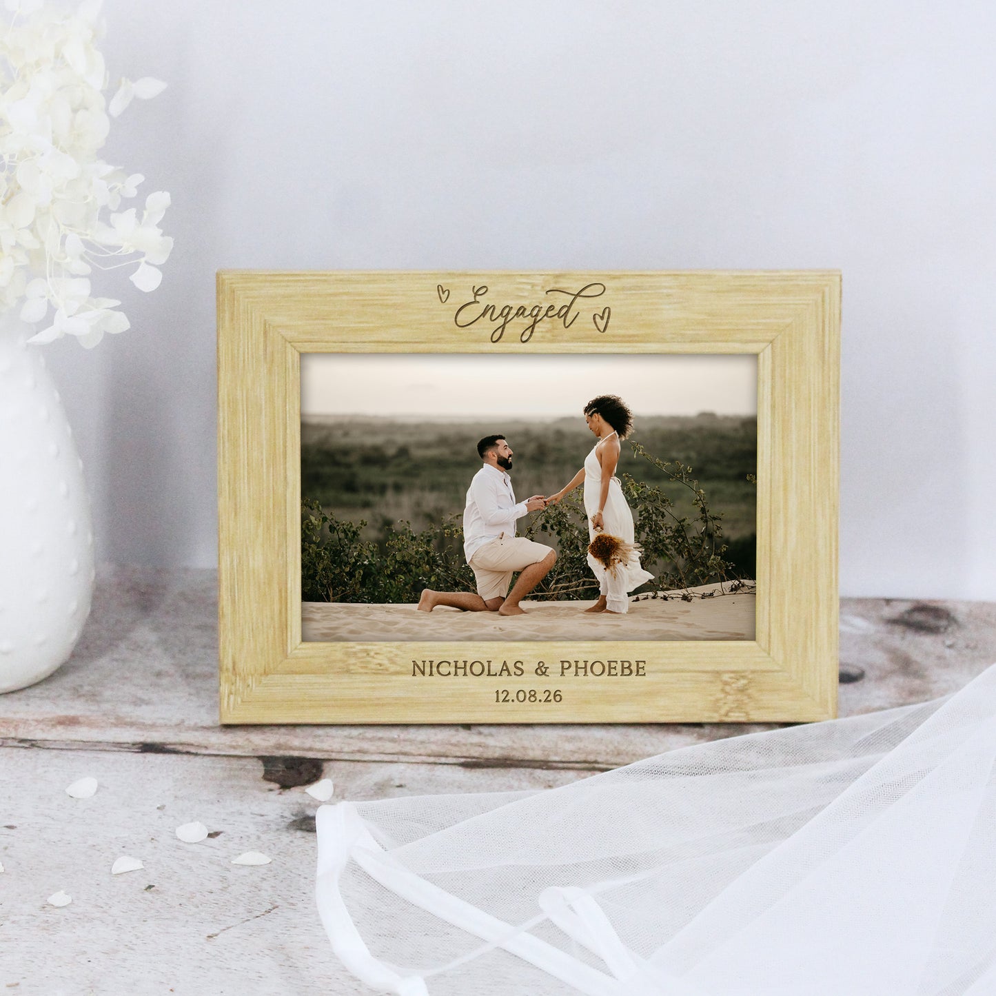 Wooden photo frame with 'Engaged' text and a couple on a beach, placed on a wooden surface.