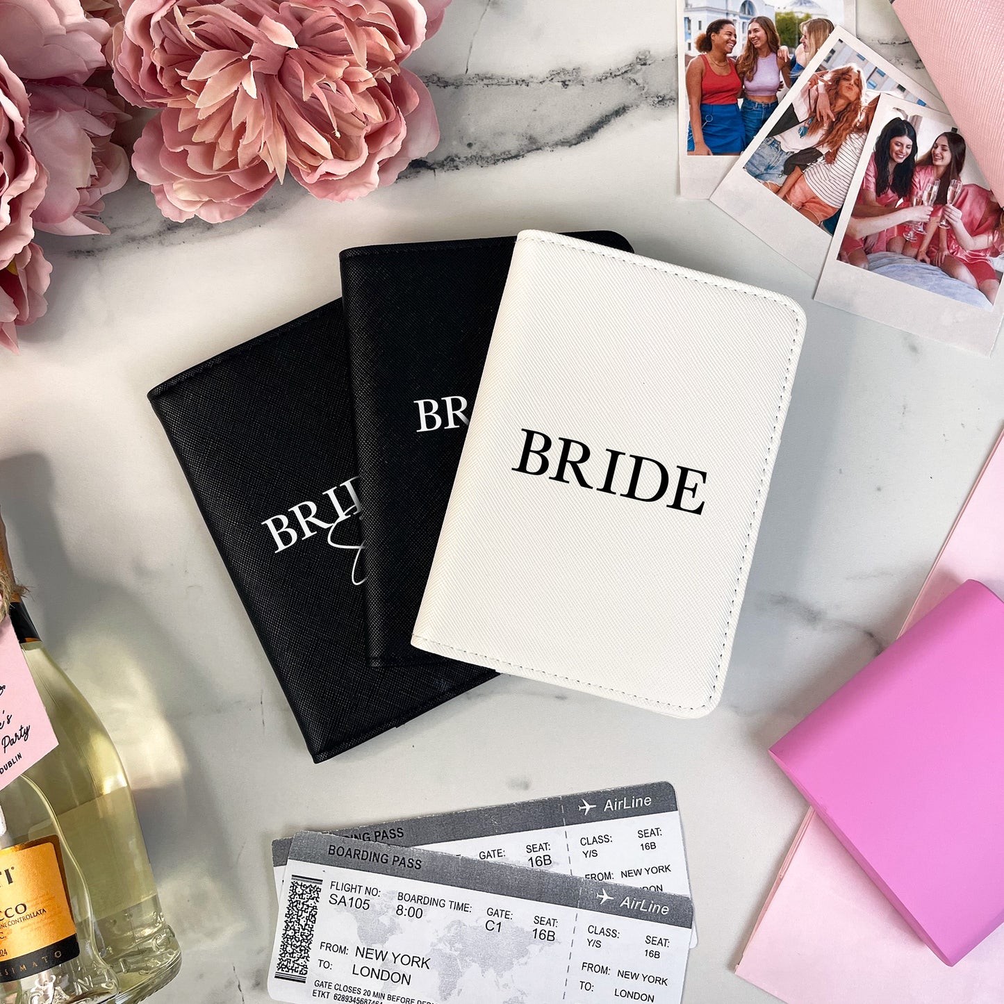 Passport covers labeled 'Bride' on a marble surface with flowers and wine bottle.