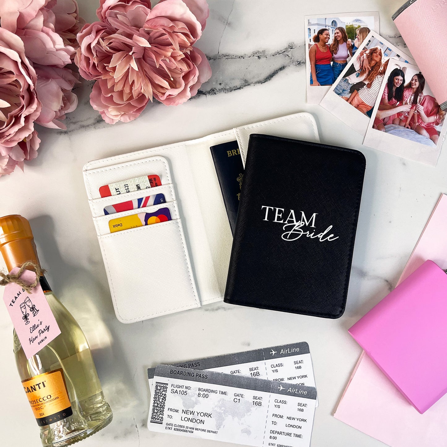 Black notebook with 'TEAM Bride' on a marble surface with flowers, wine bottle, and photos.