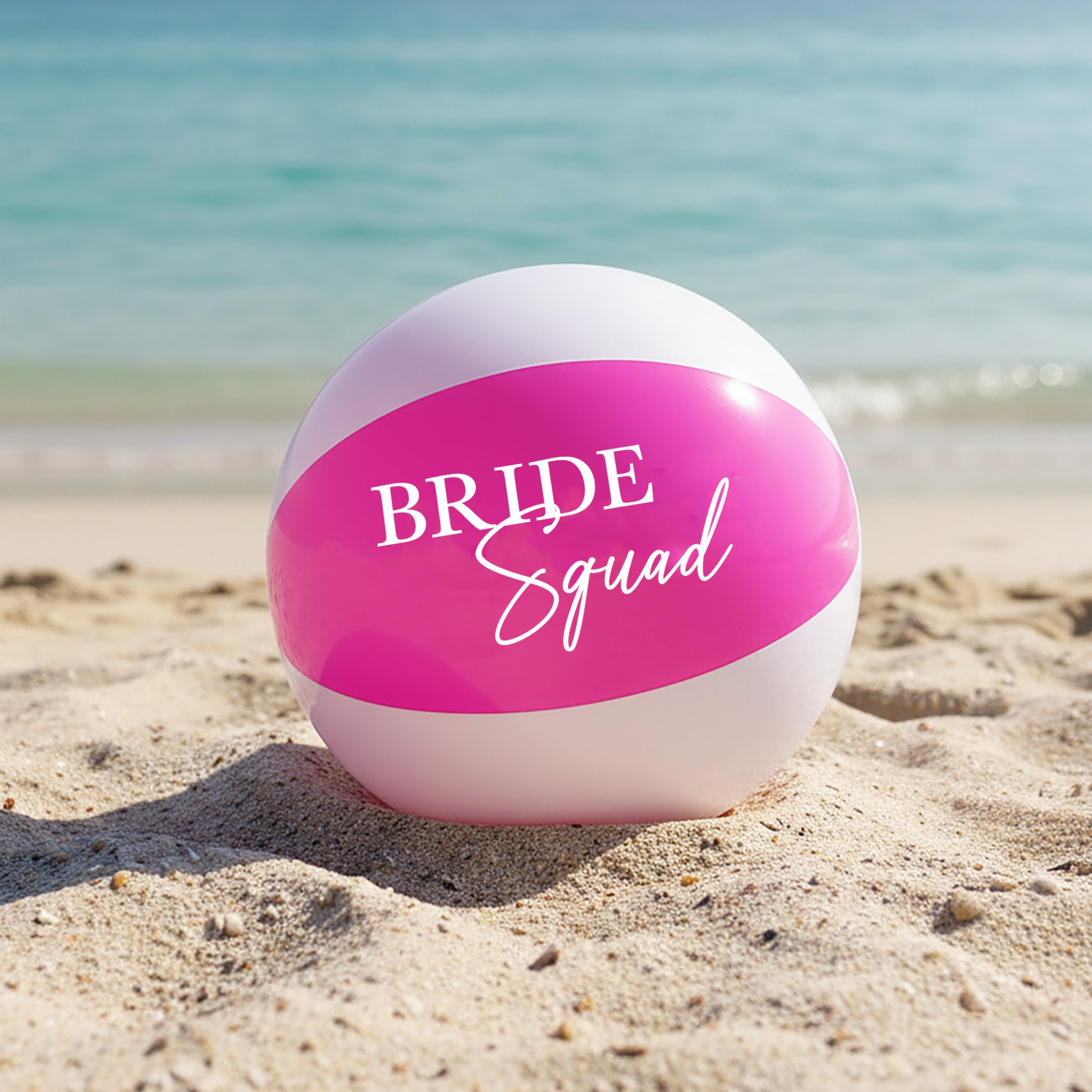 Beach ball with 'BRIDE Squad' text on a sandy beach with ocean in the background