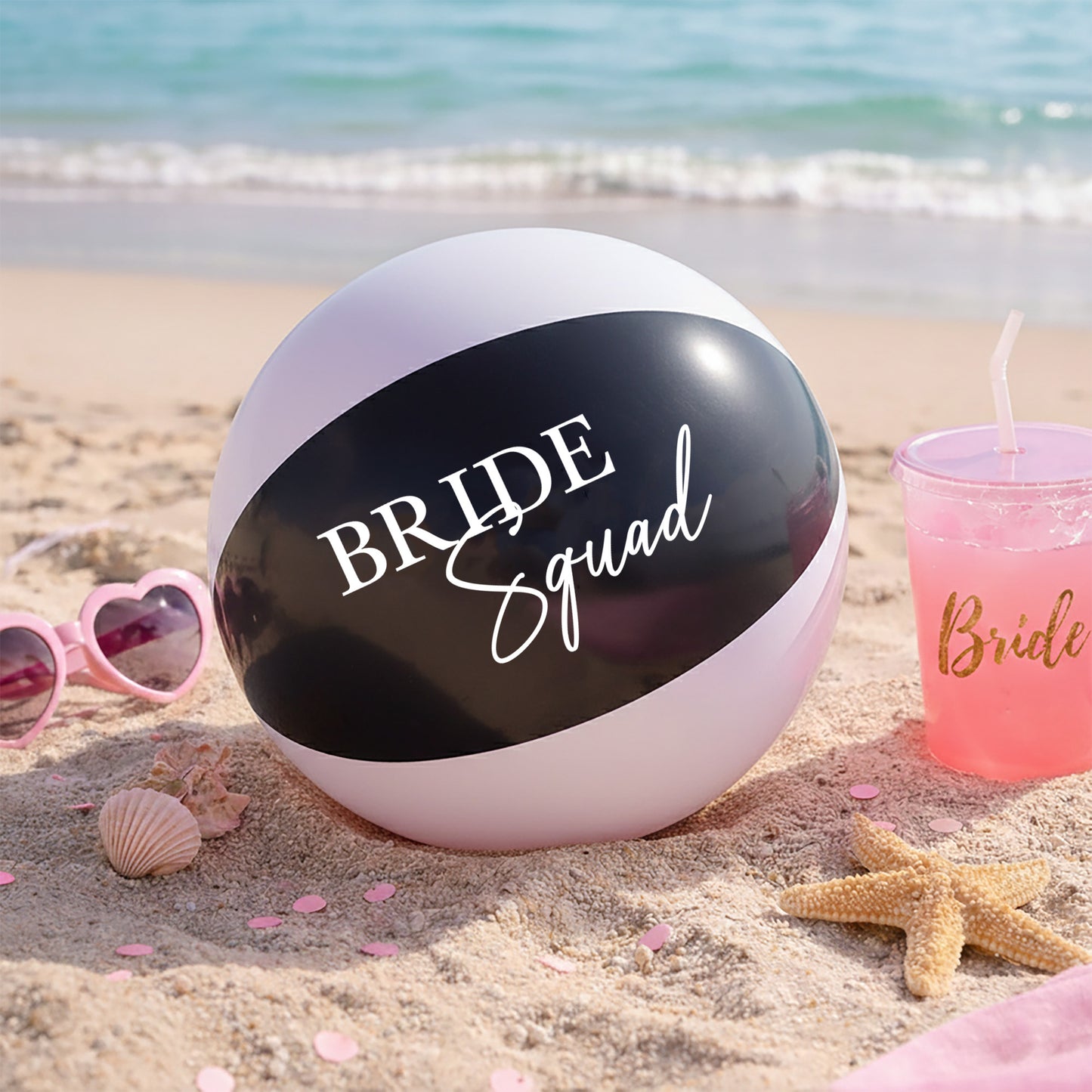 Beach ball with 'Bride Squad' text on a sandy beach with sunglasses and a cup.