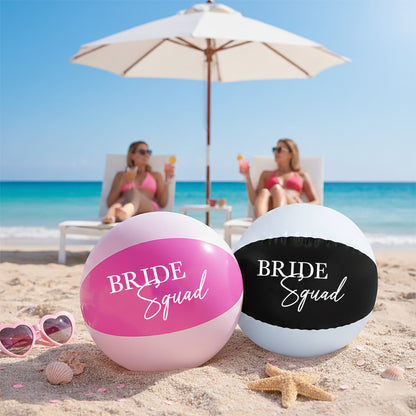 Two beach balls labeled 'Bride Squad' on a sandy beach with ocean and umbrellas in the background.