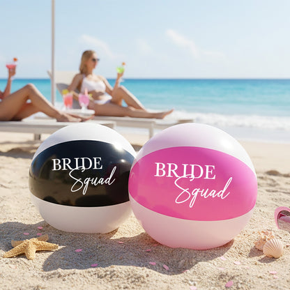 Two beach balls labeled 'Bride Squad' on a sandy beach with people in the background.