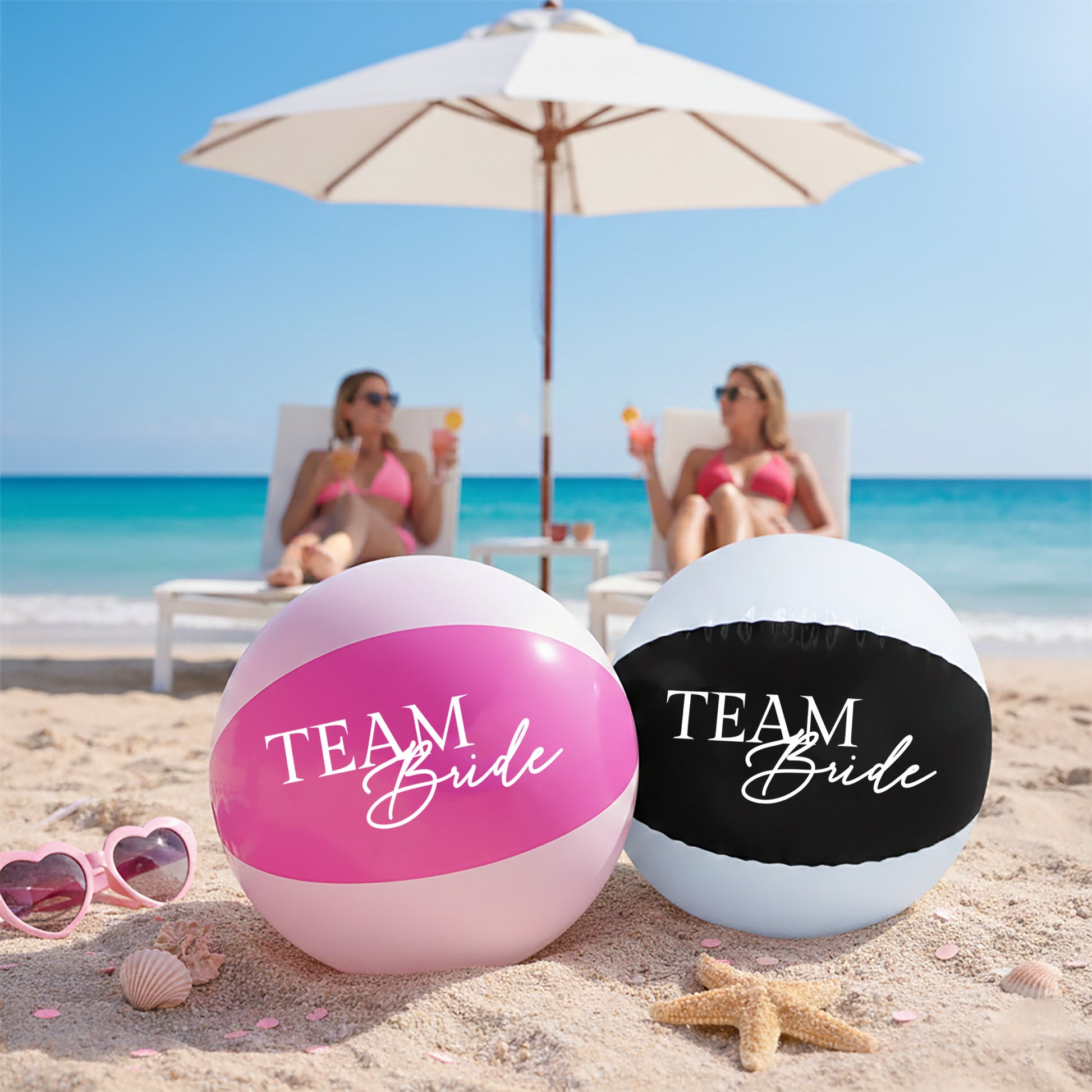 Two beach balls labeled 'Team Bride' on a sandy beach with ocean and umbrellas in the background.