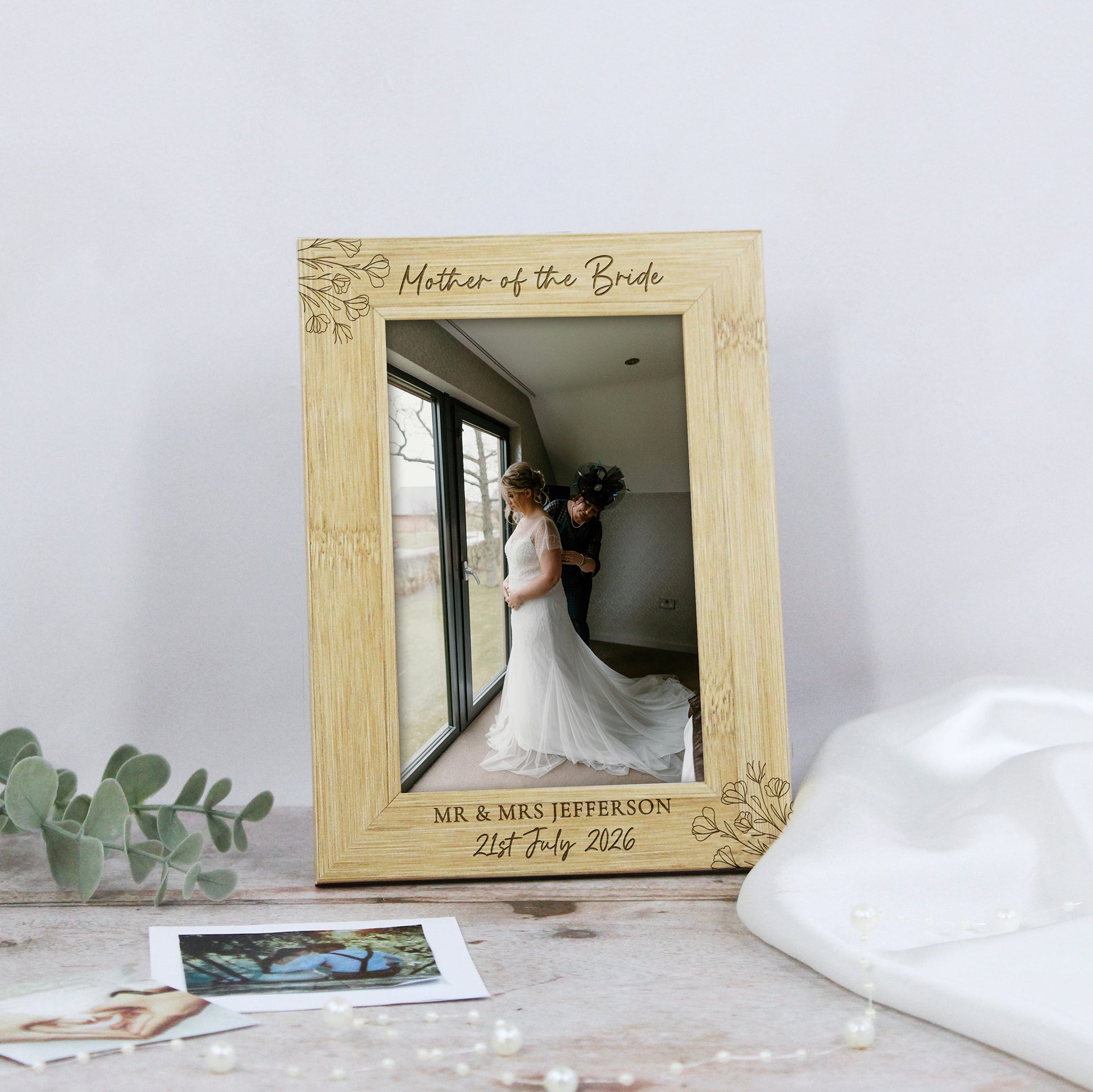 A personalized bamboo picture frame engraved with 'Mother of the Bride' and wedding details, styled on a tabletop with wedding-themed props.
