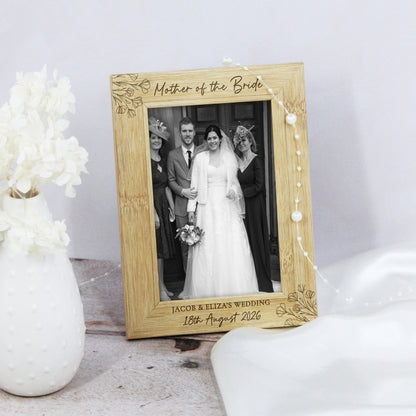 A personalized wooden picture frame with floral engravings and pearl accents, holding a black-and-white wedding photograph of a bride and groom. The frame is styled on a tabletop next to a white vase with flowers.