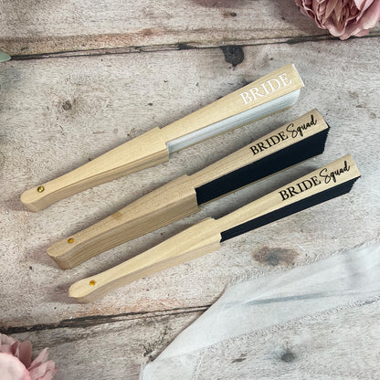 Three wooden fans with 'Bride' and 'Bride Squad' text on a rustic wooden surface.