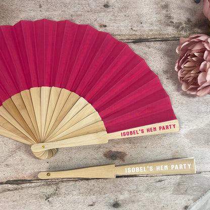 Red and gold fans with 'Isobel's Hen Party' text on a wooden surface.