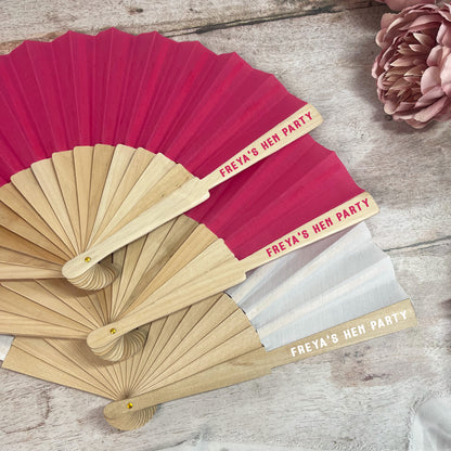 Set of personalized hand fans with 'FREYA'S HEN PARTY' text on a wooden surface.