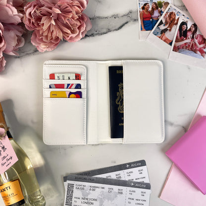 White wallet with travel documents on a marble surface with flowers and a bottle of wine.