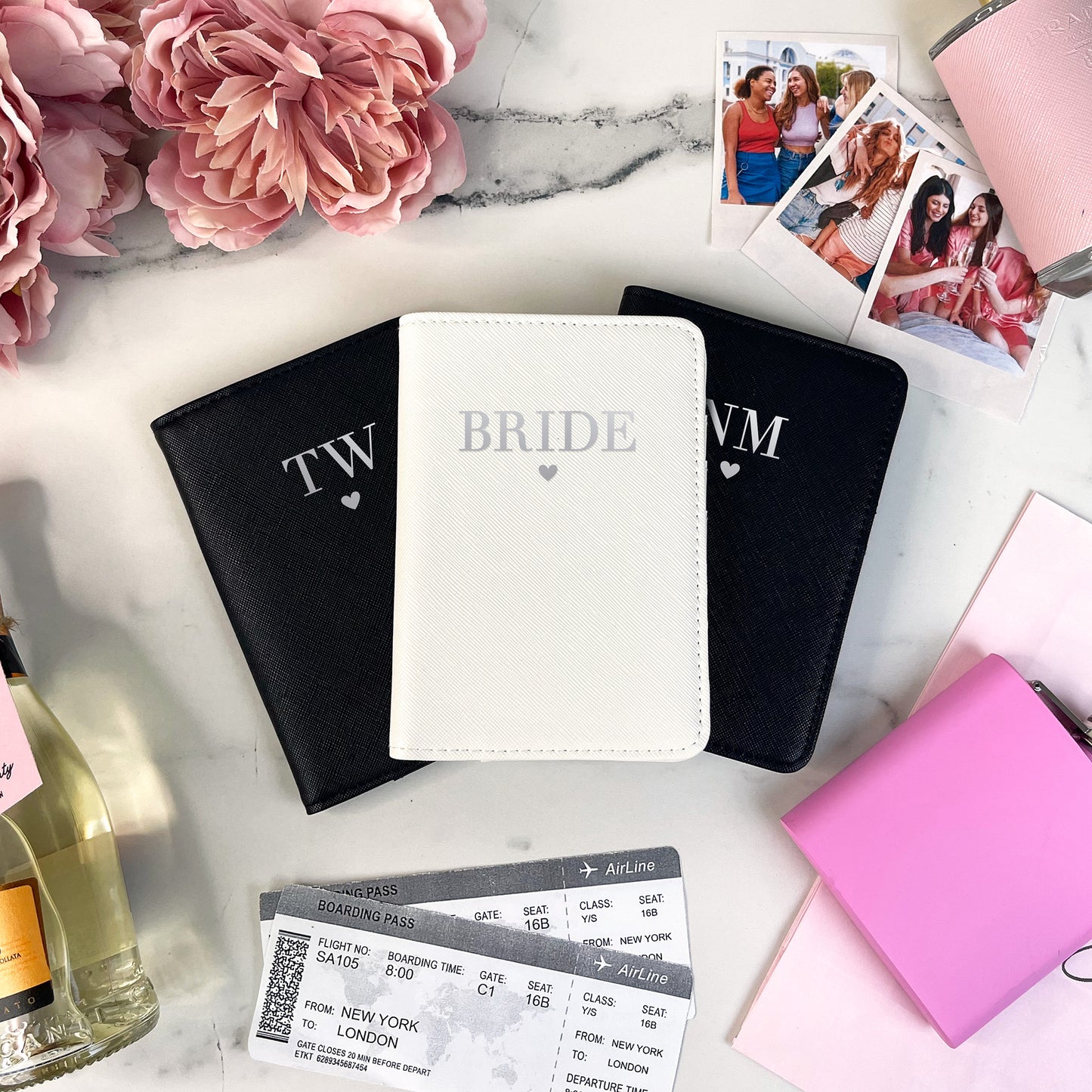 Three passport covers with initials 'TW', 'BRIDE', and 'WIM' on a marble surface with flowers and photos.