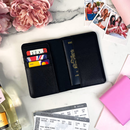 Black passport holder with travel documents on a marble surface with flowers and a bottle.