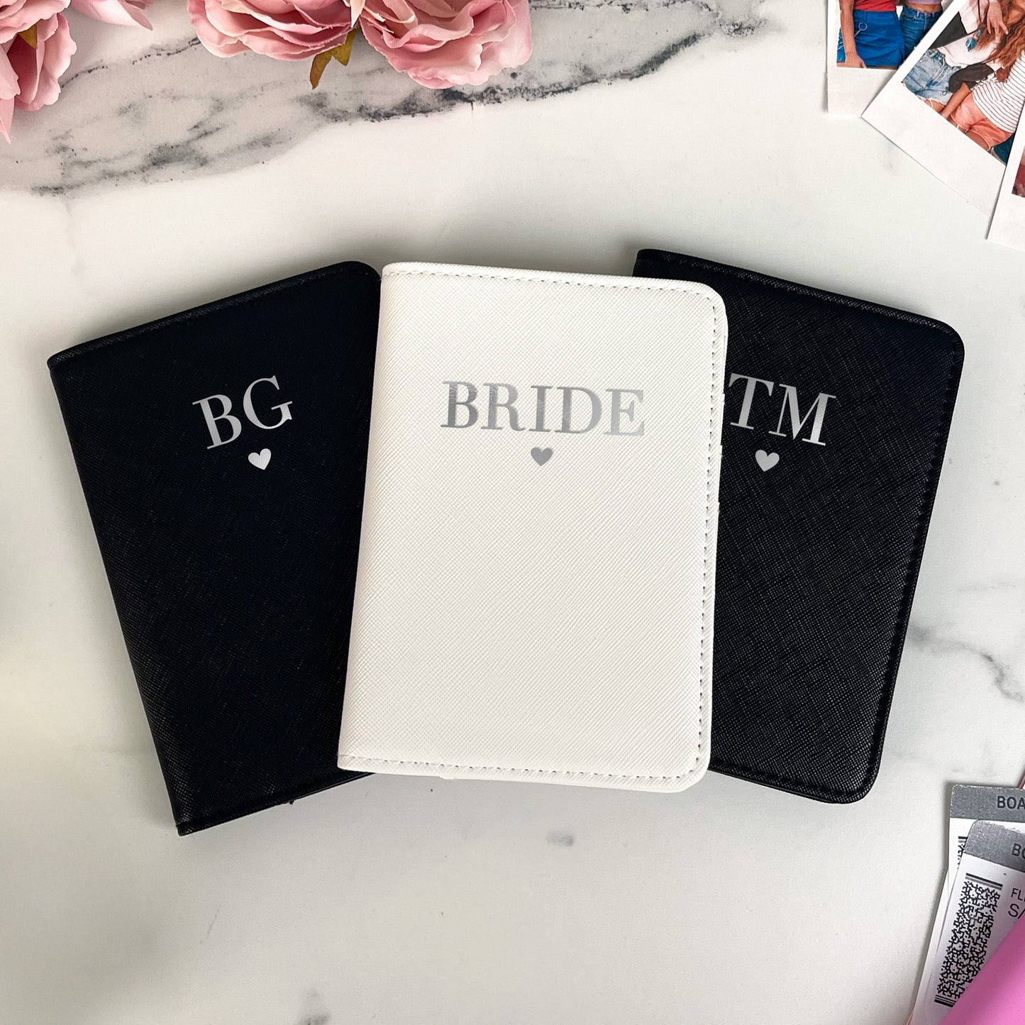 Three personalized passport covers on a marble surface with flowers and a card in the background.