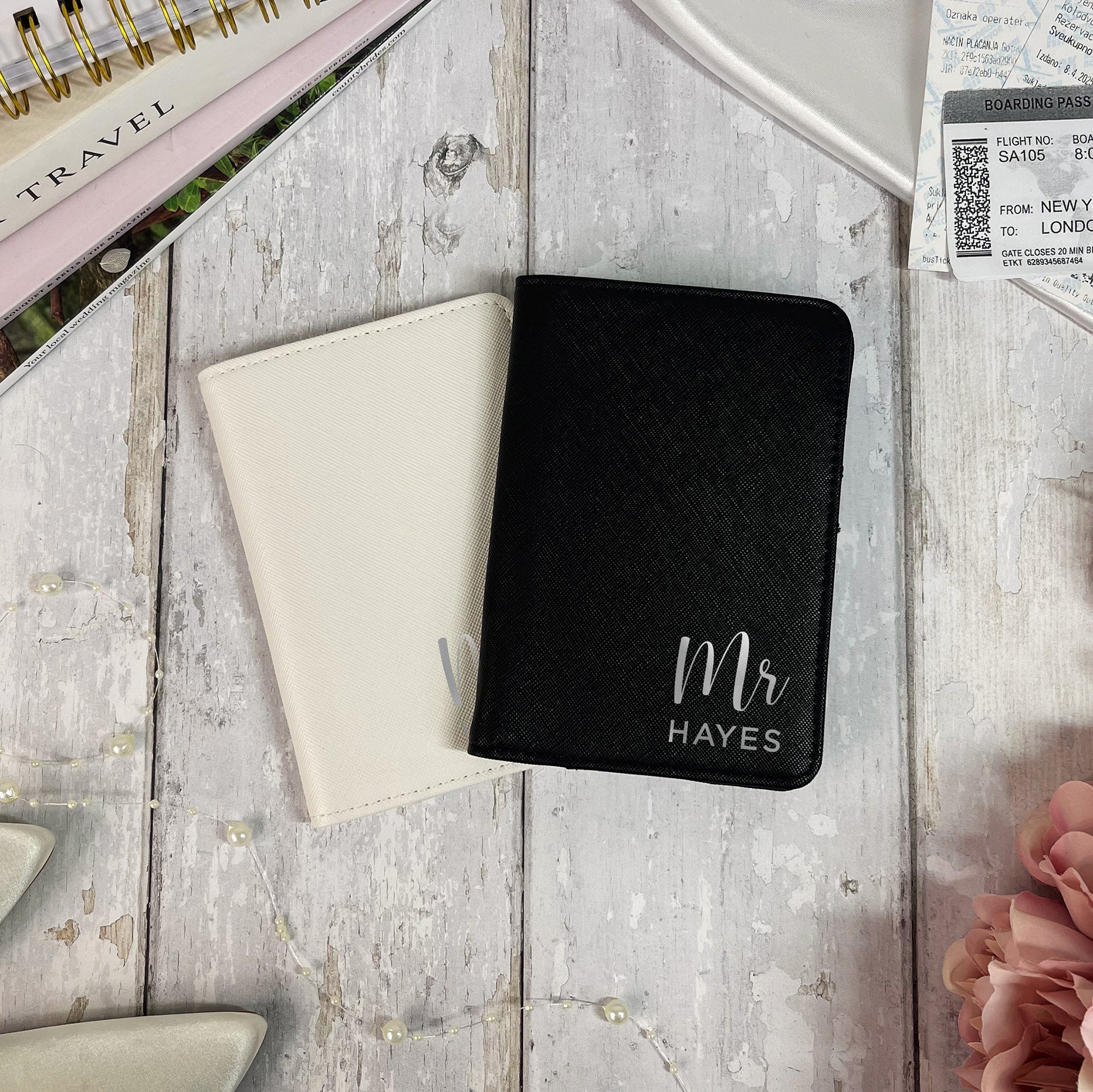 Black passport holder with 'Mr Hayes' text on a wooden surface with travel items.