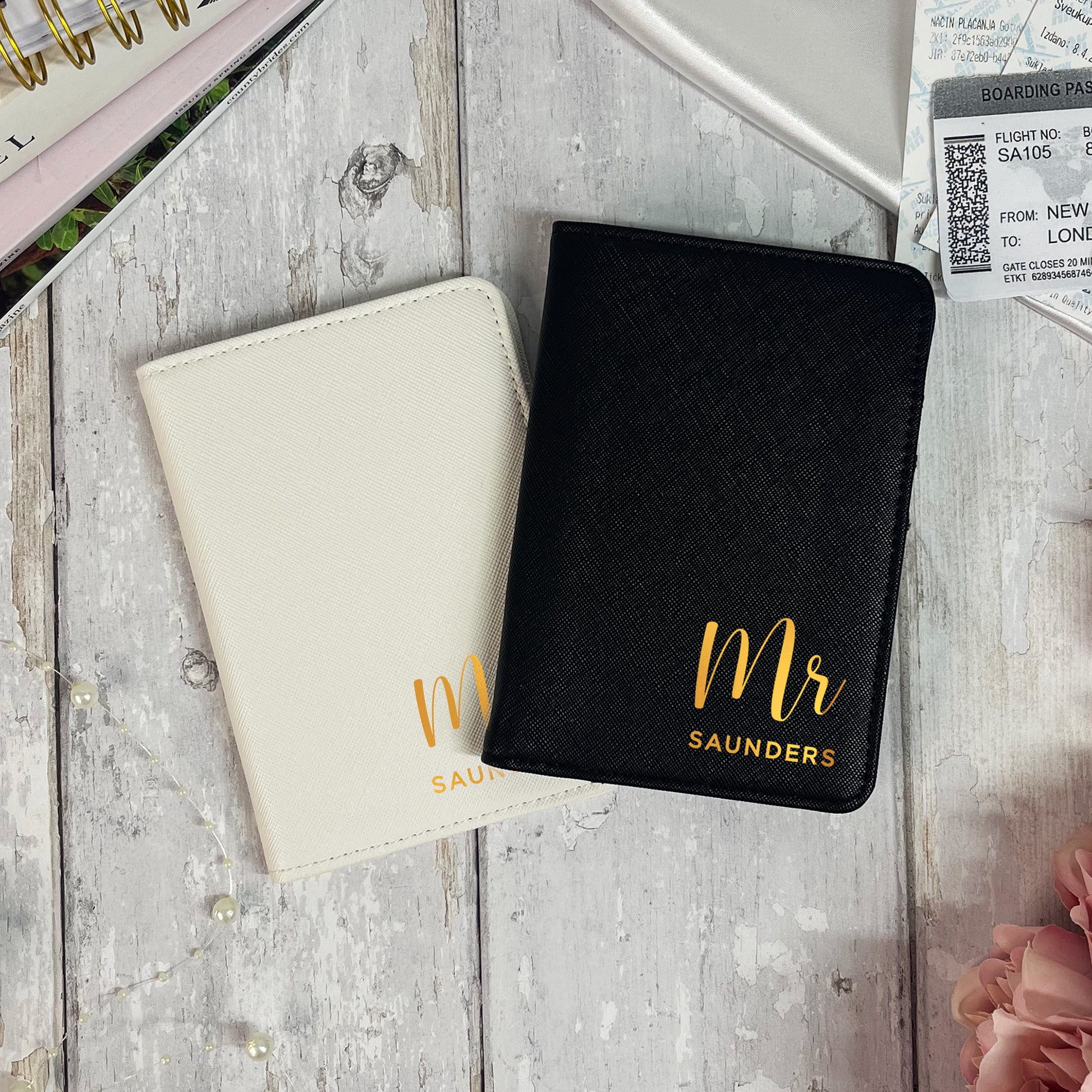 Two passport holders, one beige and one black, with 'Mr Saunders' text on a wooden surface.