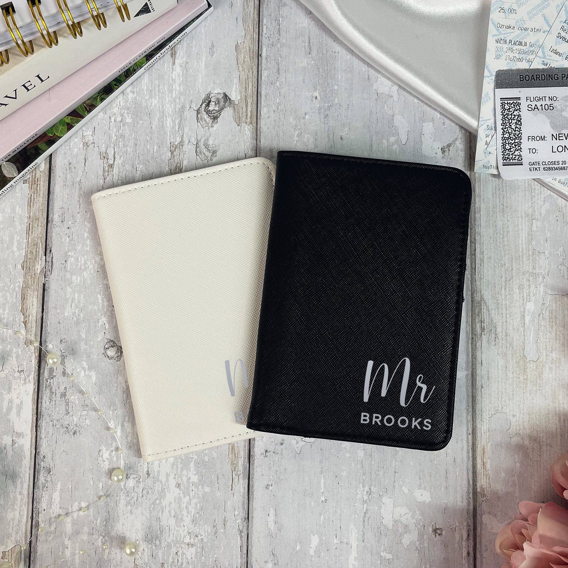 Two passport holders, one black with 'Mr Brooks' text and one beige, on a wooden surface.