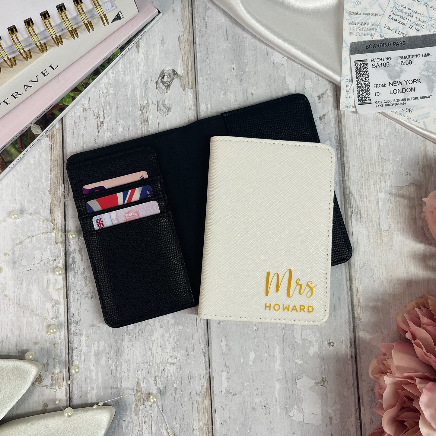 Black wallet with cards and a white passport holder with 'Mrs Howard' on a wooden surface.