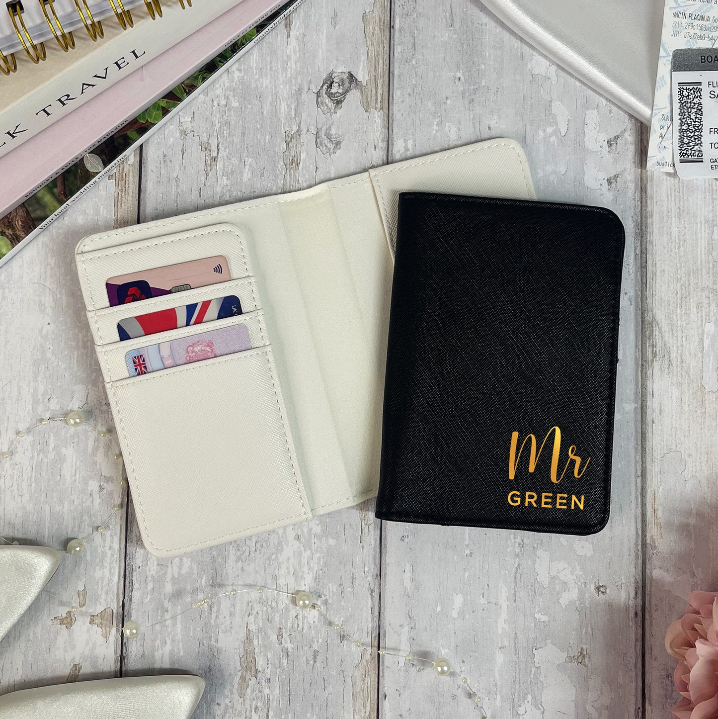 Black passport holder with 'Mr Green' text on a wooden surface with travel items.