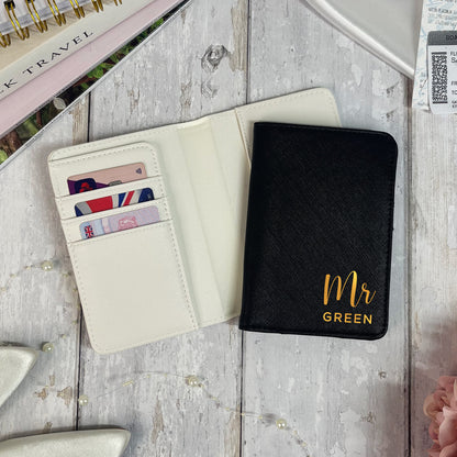 Black passport holder with 'Mr Green' text on a wooden surface with travel items.
