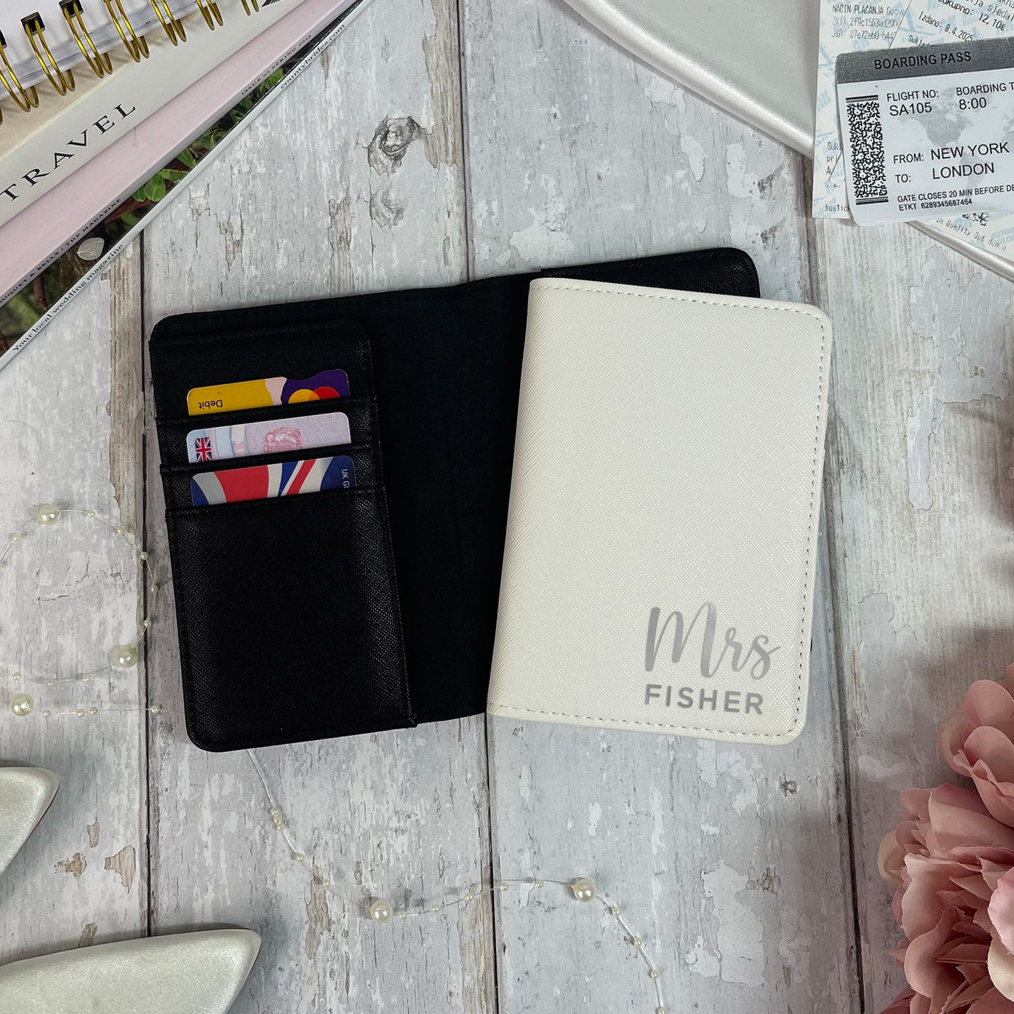 Black wallet with colorful cards and white passport holder with 'Mrs Fisher' engraving on a textured surface.