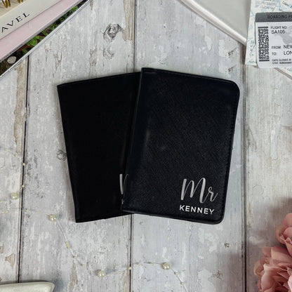 Two black passport holders on a wooden surface with 'Mr Kenney' text.