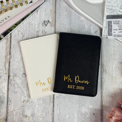 Two passport holders, one black and one beige, with personalized text on a wooden surface.