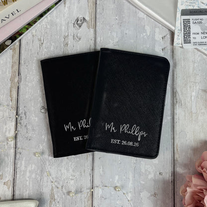 Two black passport holders with 'Mr. Phillips' text on a wooden surface.