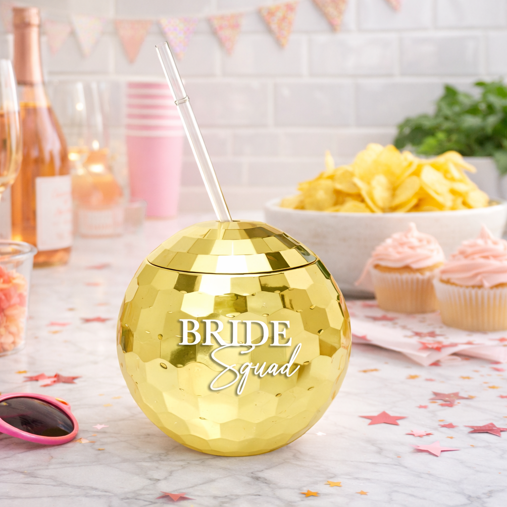 Gold disco ball with 'Bride Squad' text on a table with snacks and drinks.
