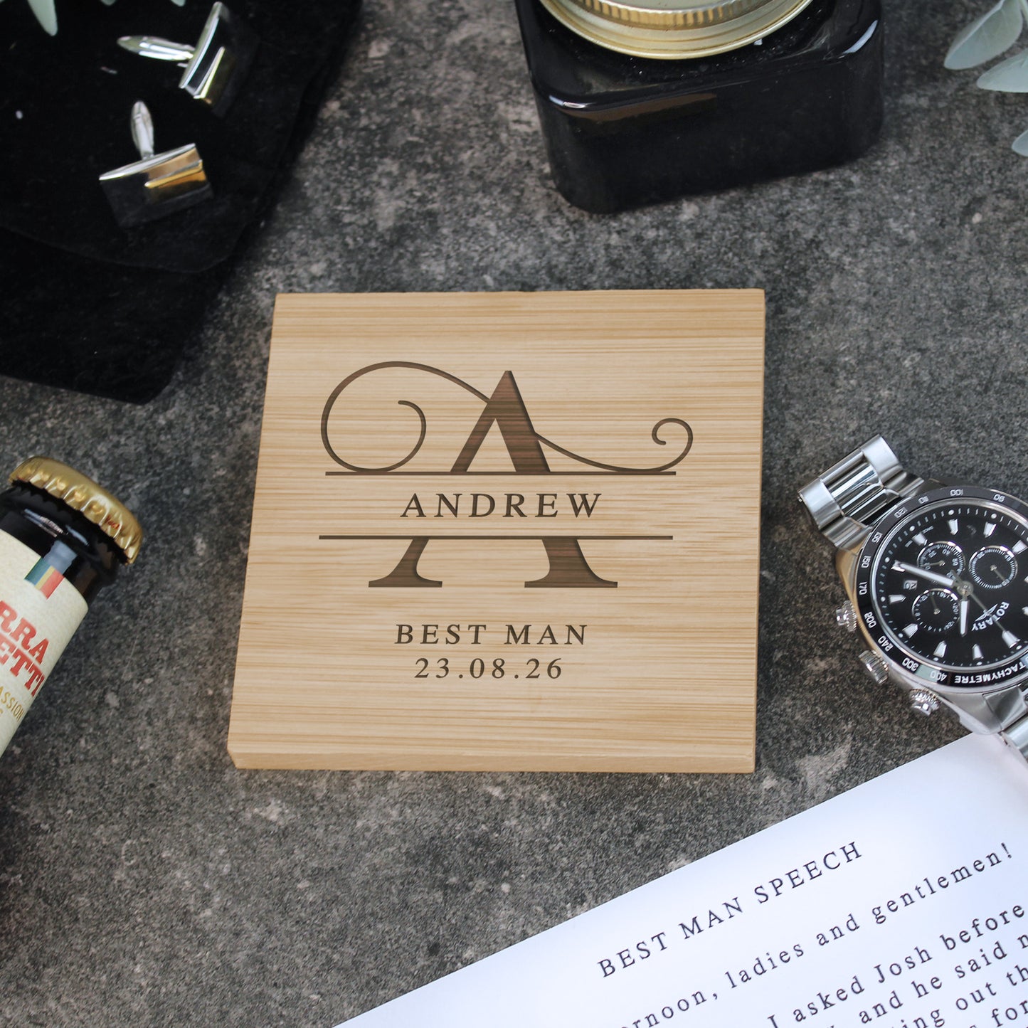 Wooden coaster with engraved name and date on a concrete surface with stationery items.