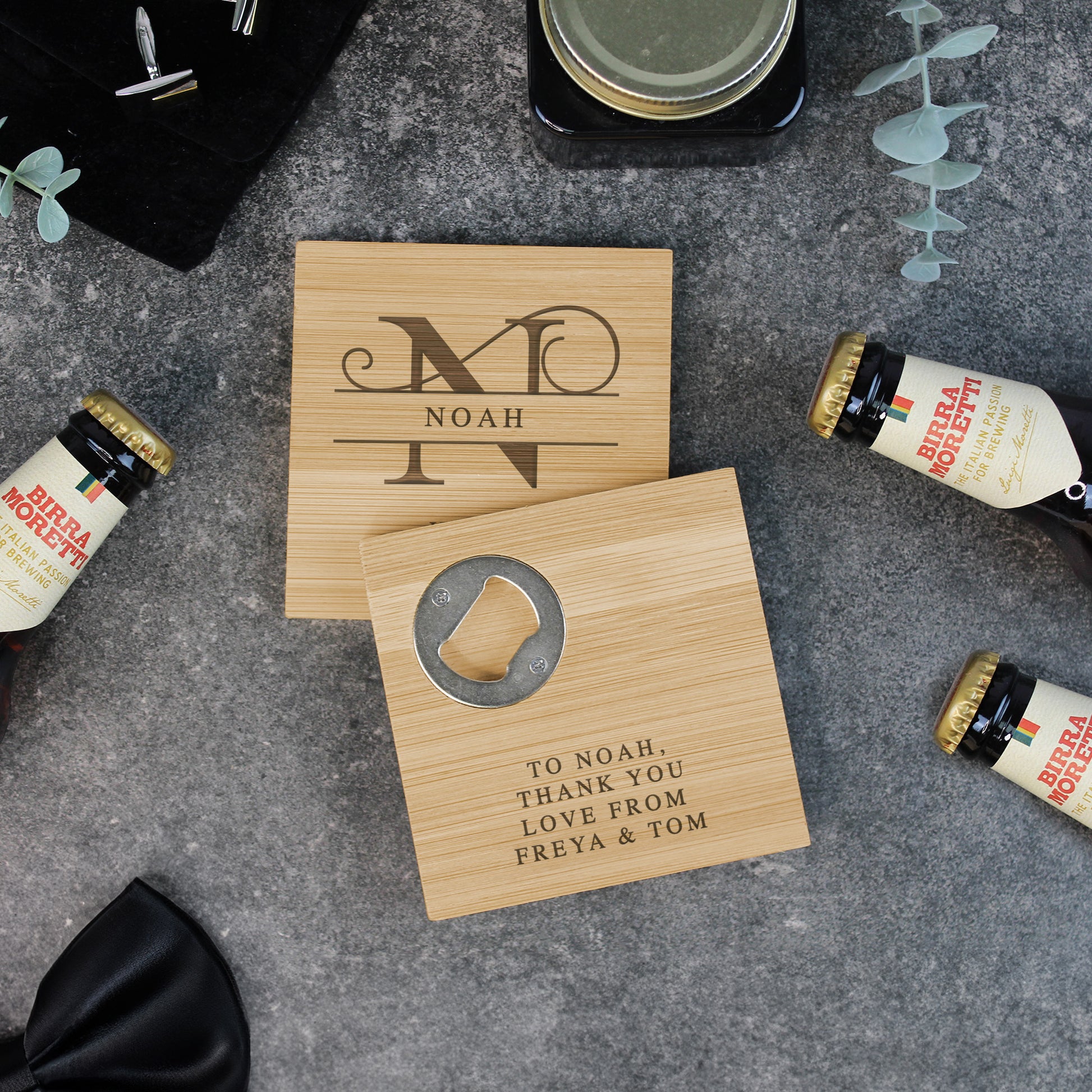 Two wooden coasters with engraved text on a gray surface with beer bottles.