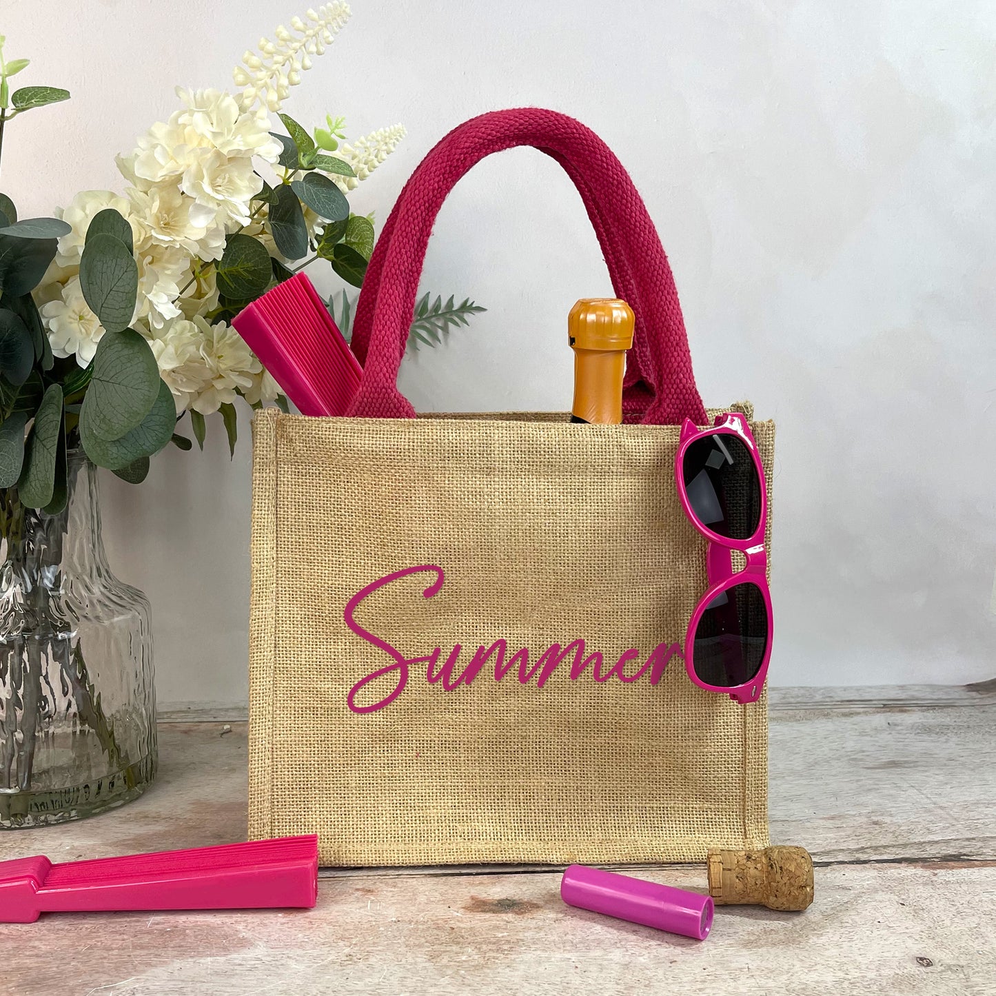 Beige tote bag with 'Summer' text, pink sunglasses, and bottle accessories on a wooden surface.