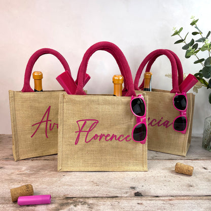 Three jute bags with pink handles and sunglasses, on a wooden surface with a light background.