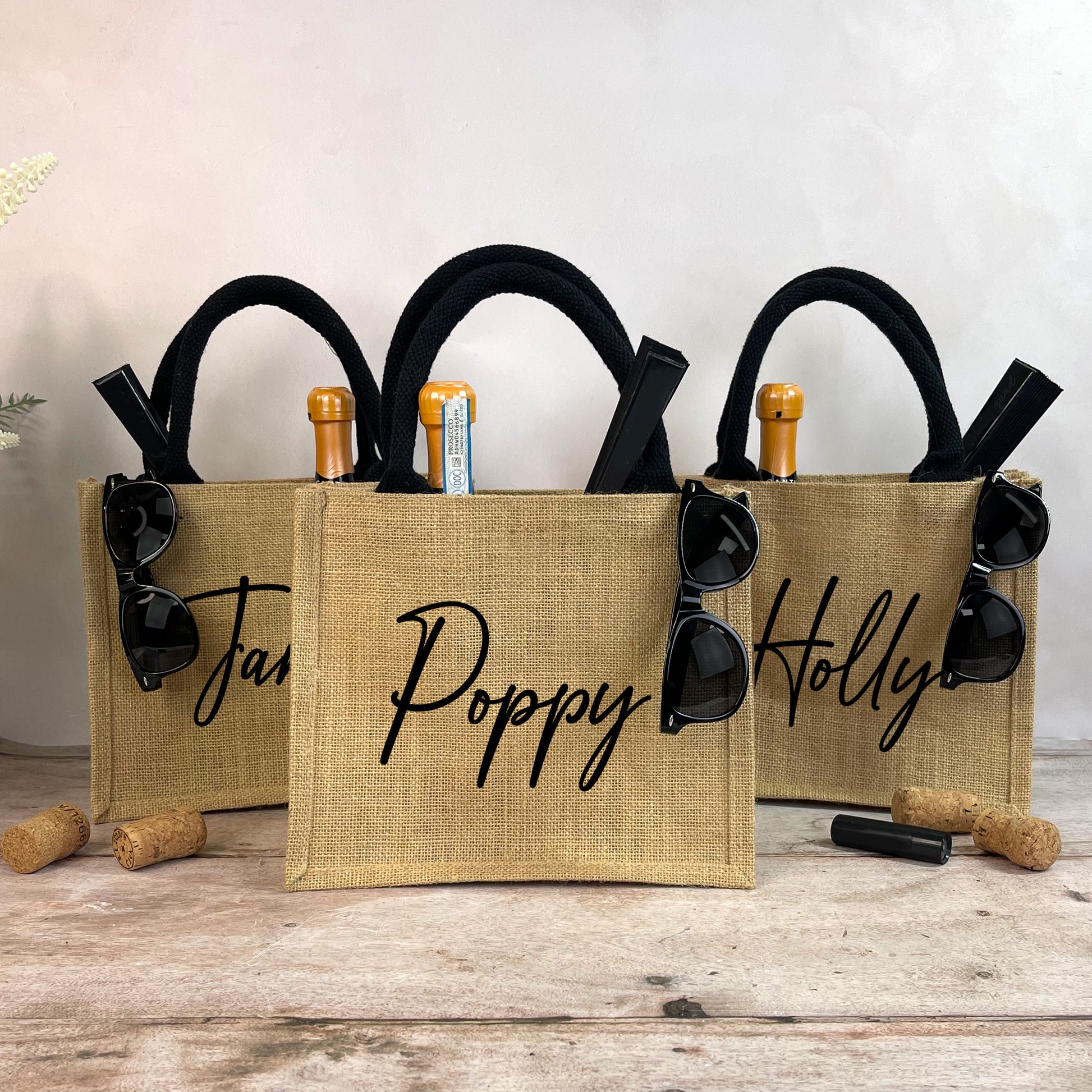 Three burlap bags with sunglasses and wine bottle holders on a wooden surface.