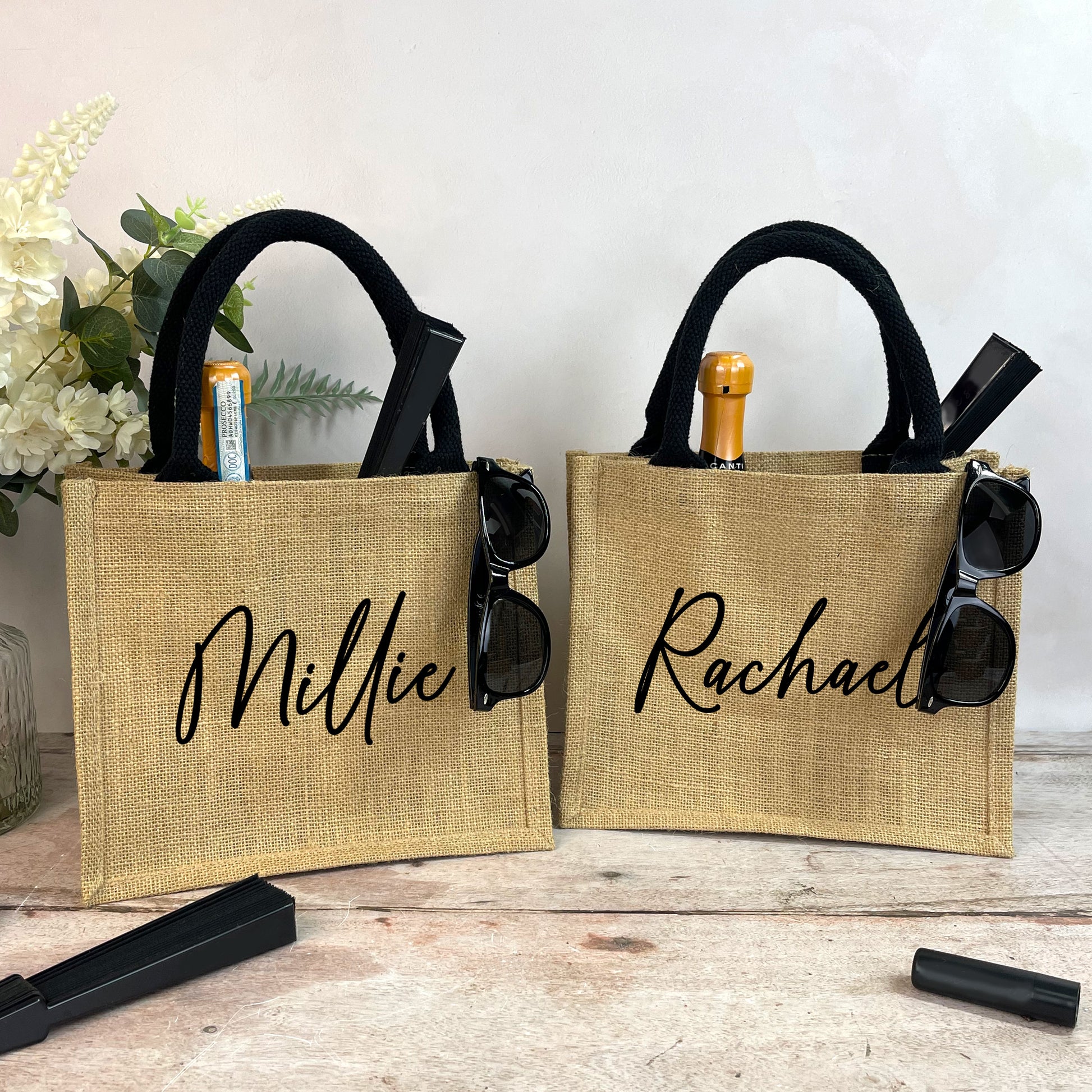 Two jute bags with personalized names 'Millie' and 'Rachael' on a wooden surface.