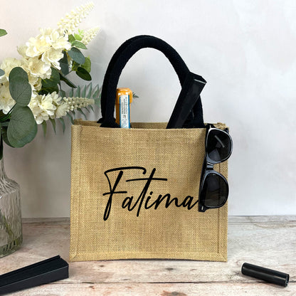 Jute bag with 'Fatima' branding on a wooden surface with flowers in the background