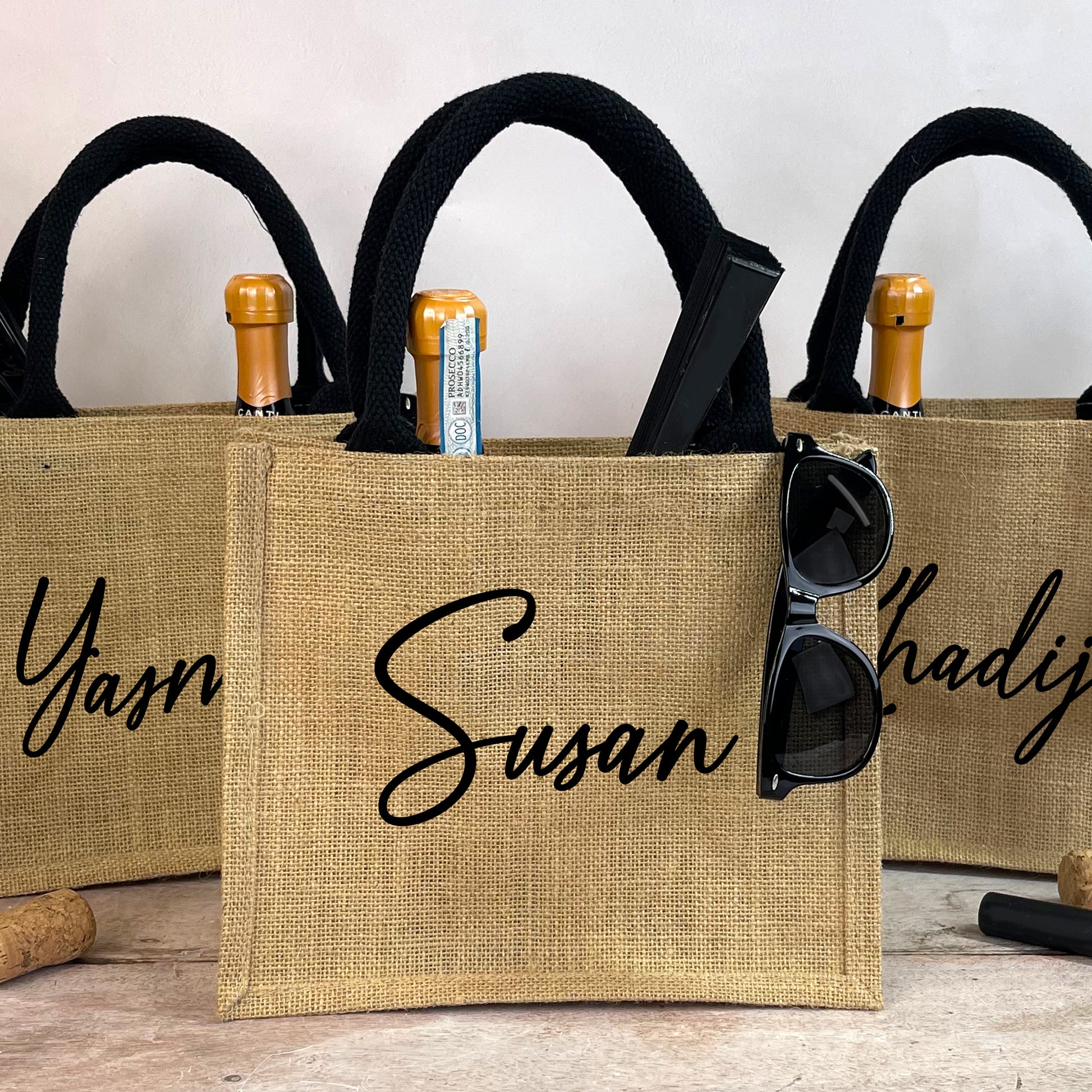 Three burlap bags with personalized names 'Yasmin', 'Susan', and 'Hadija' on a wooden surface.