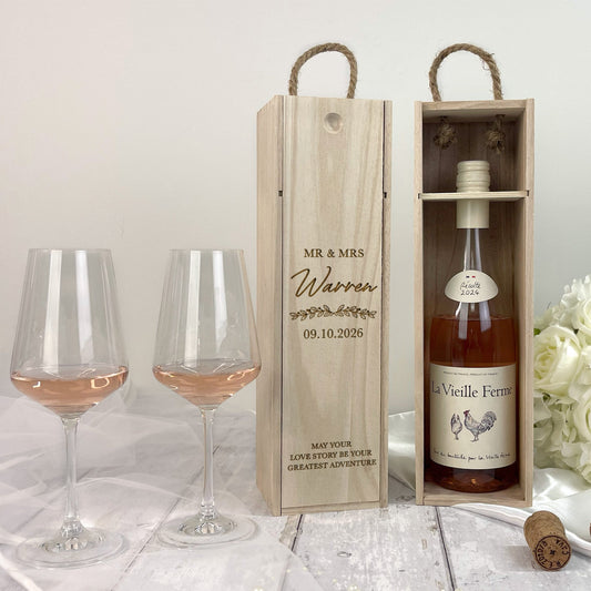 Wine bottle in a wooden box with glasses and flowers on a light background