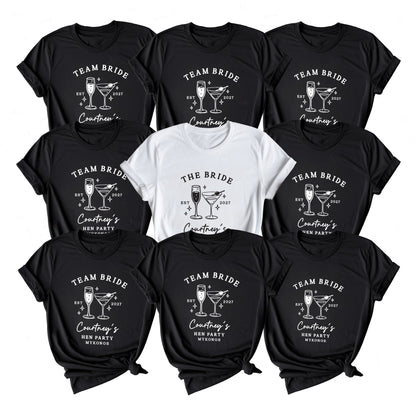 Nine black short-sleeve graphic T-shirts arranged in a 3x3 grid, with one white shirt centered. The shirts feature white printed graphics of cocktail glasses and text including 'TEAM BRIDE', 'The Bride', and 'Courtney's New Party Everything'.