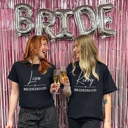 Two women wearing 'Bridesmaid' shirts with 'BRIDE' balloons in the background.