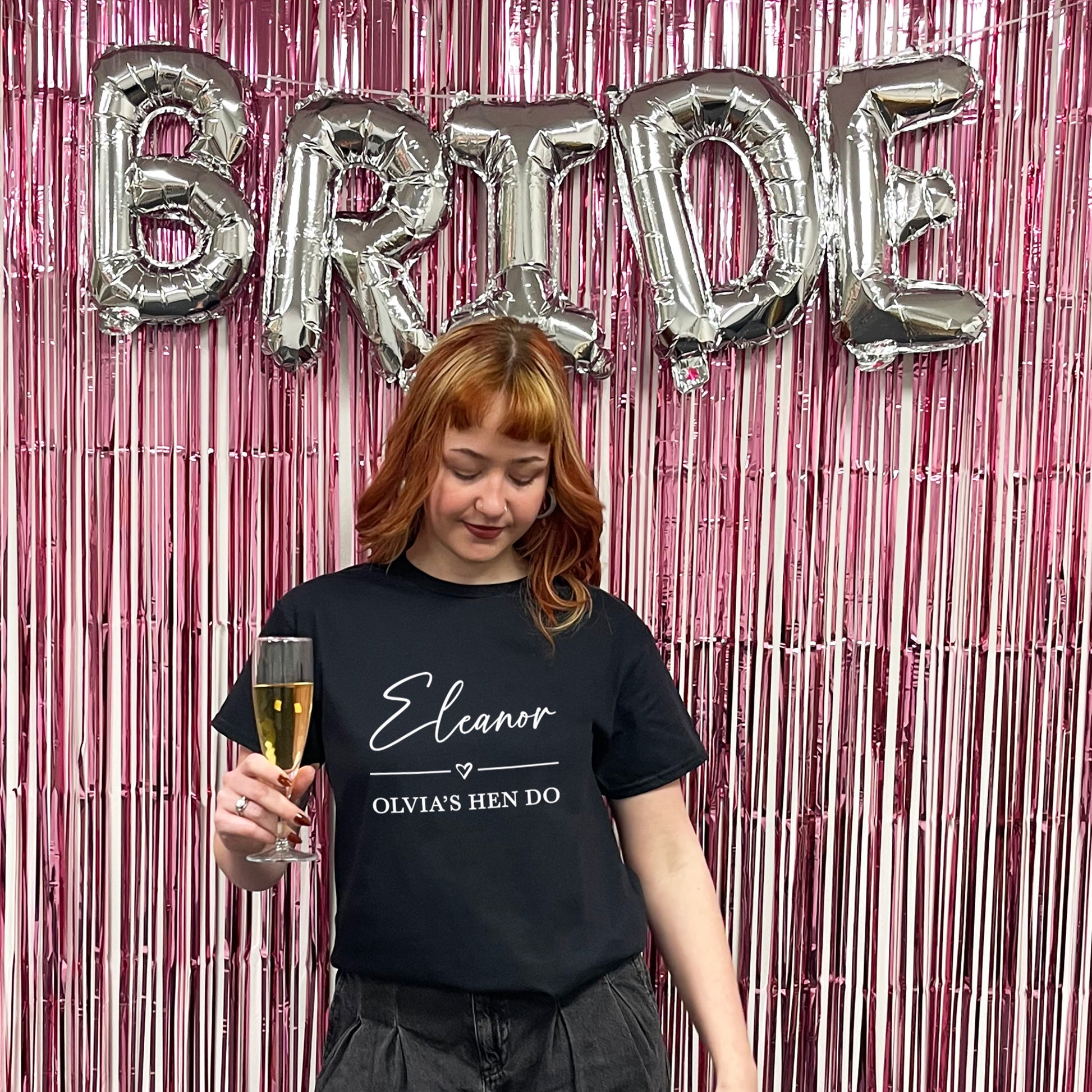Woman holding a glass of champagne with 'BRIDE' balloons and pink streamers in the background