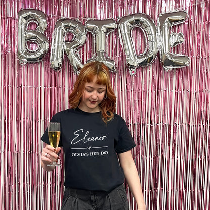 Woman holding a glass of champagne with 'BRIDE' balloons and pink streamers in the background