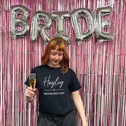 Woman holding a glass of champagne with 'BRIDE' balloons and pink tinsel in the background