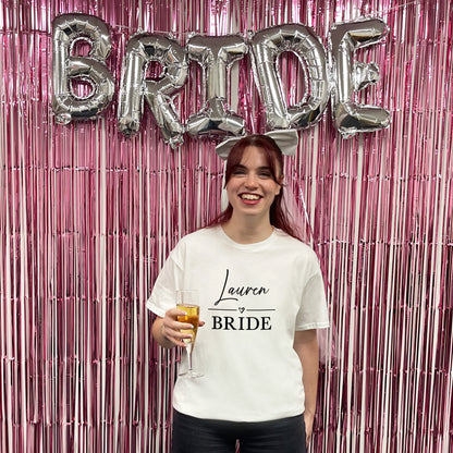 Woman in a 'Lauren Bride' t-shirt with 'BRIDE' balloons and pink fringe curtain