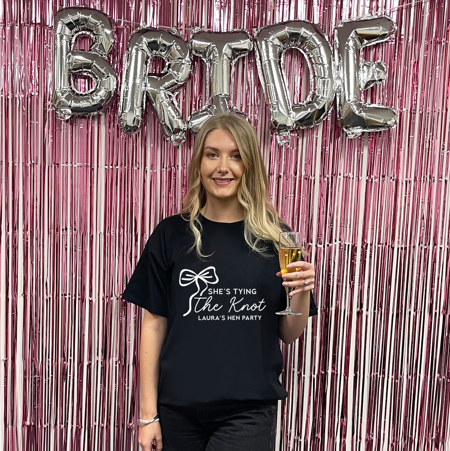 Woman holding a glass of beer in front of 'BRIDE' balloons and pink streamers.