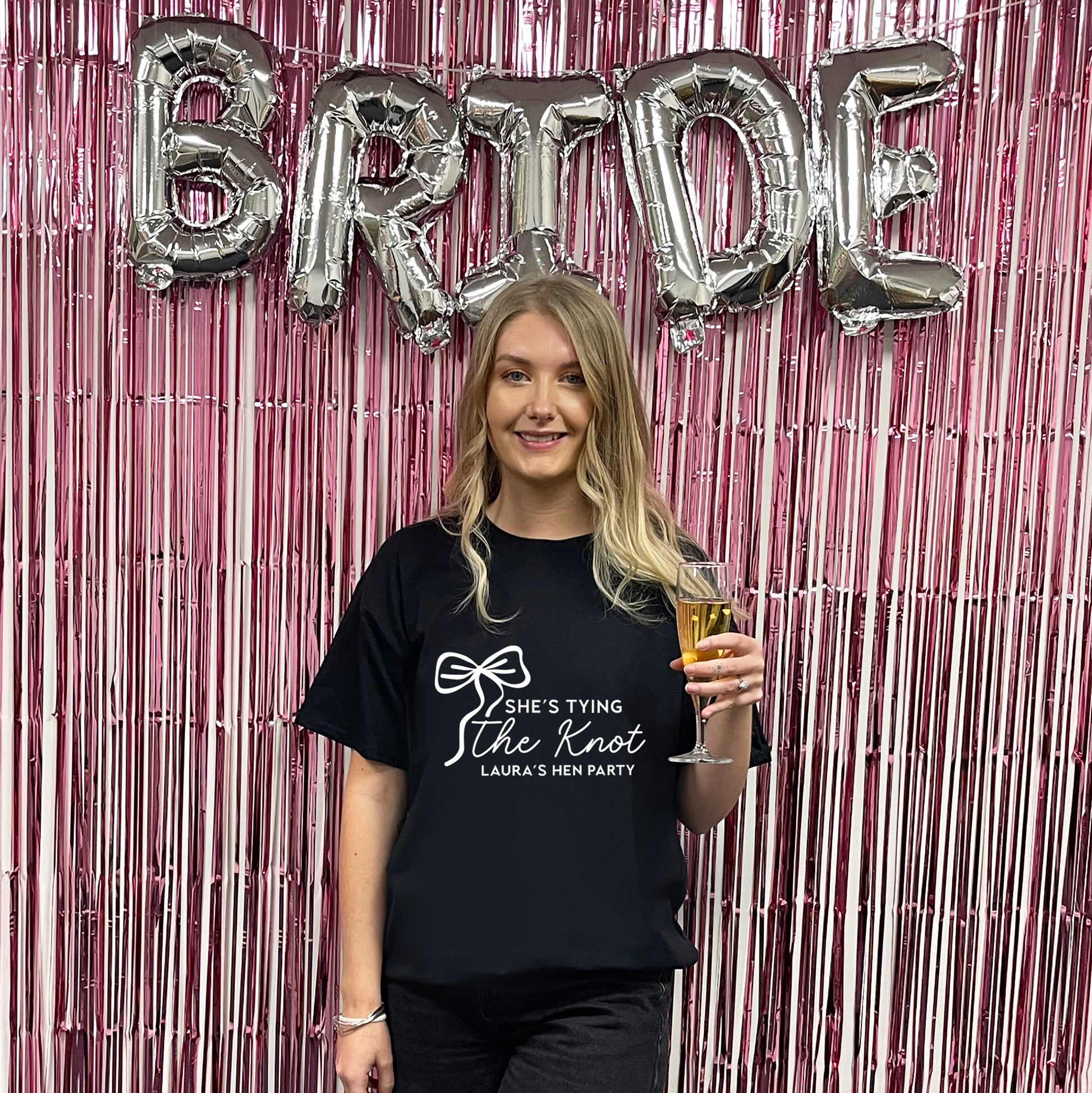 Woman holding a glass of beer in front of 'BRIDE' balloons and pink streamers.