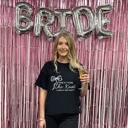 Woman holding a glass of beer in front of 'BRIDE' balloons and pink streamers.