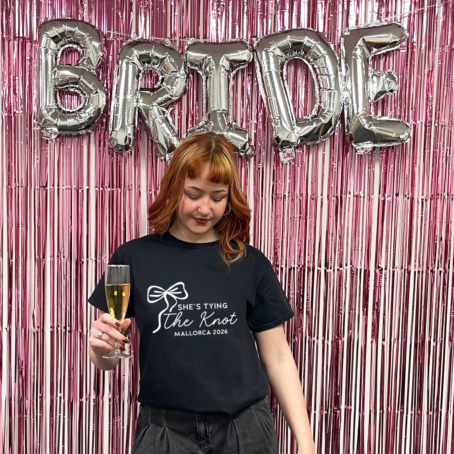 Woman holding a glass of champagne with 'Bride' balloons and pink tinsel in the background