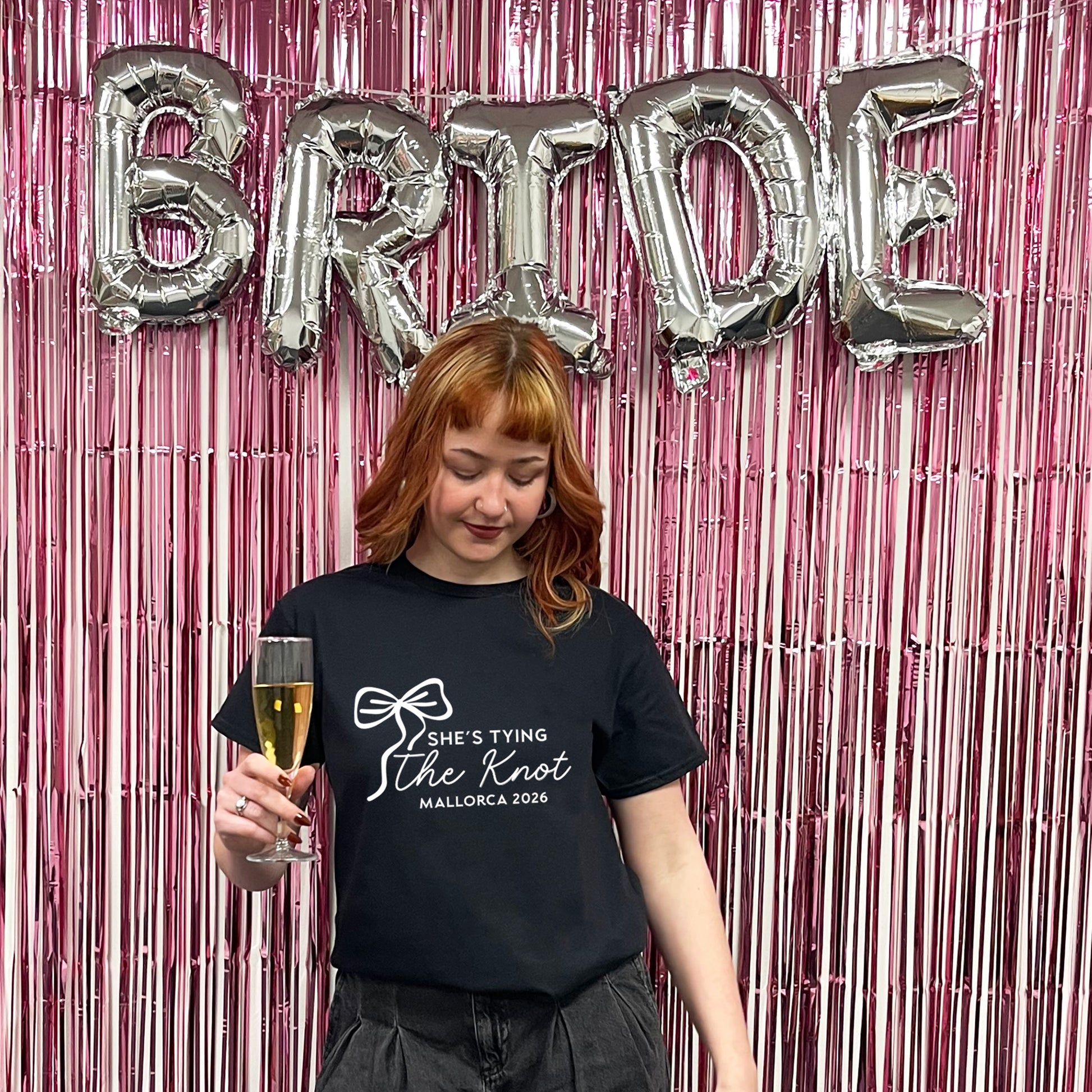 Woman holding a glass of champagne with 'Bride' balloons and pink tinsel in the background
