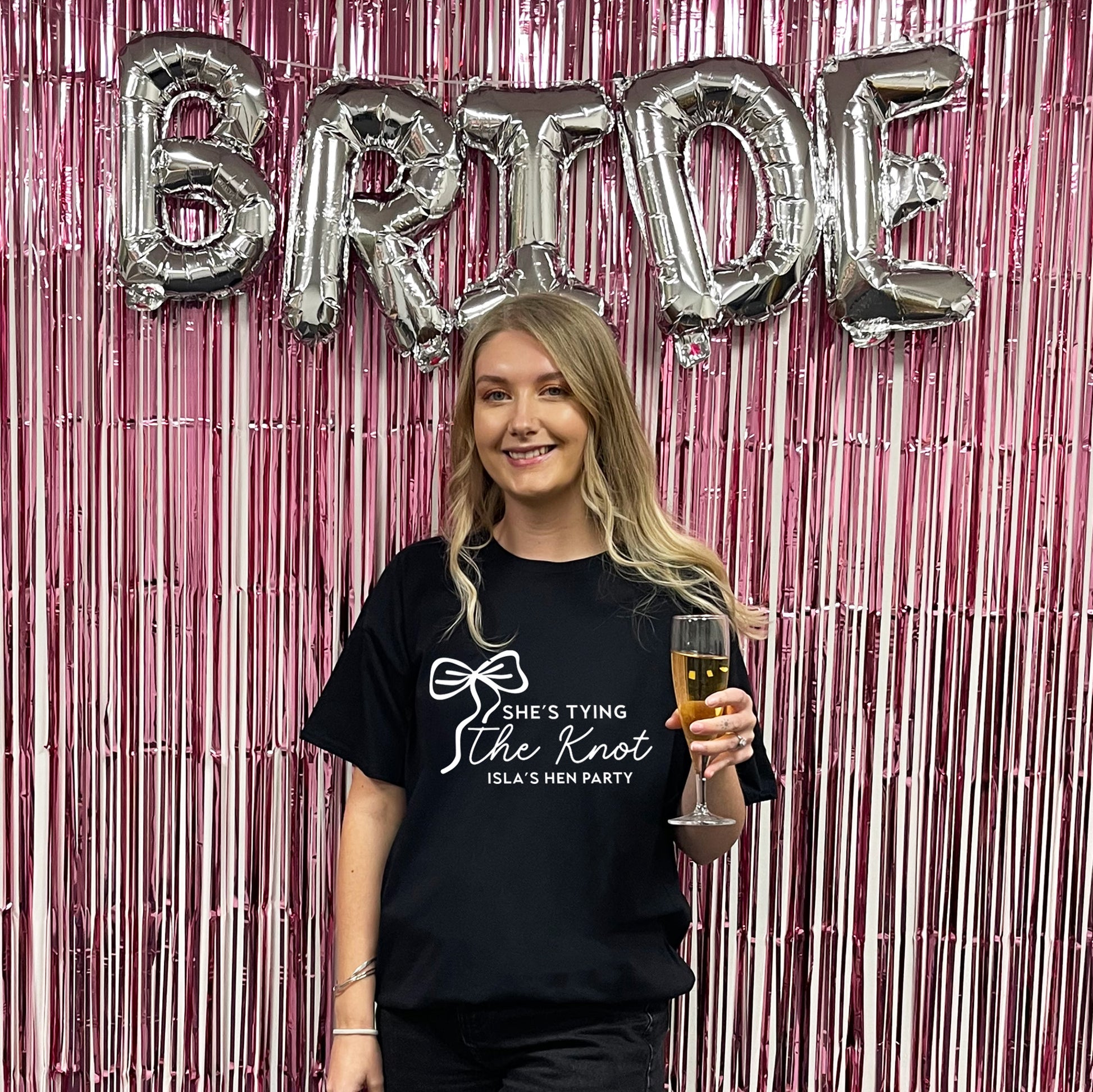 Woman holding a glass of champagne with 'Bride' balloons and pink tinsel in the background